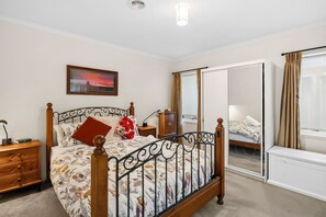 A bedroom with a bed, a nightstand, a dresser, a mirror, and a window with curtains. - Beach Living Bliss (Torquay)
