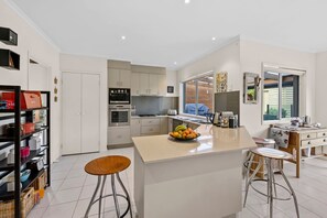 A modern kitchen with a central island, stainless steel appliances, and a view to the outside. - Beach Living Bliss (Torquay)