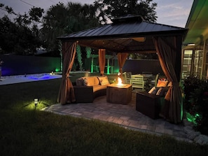 An outdoor patio with a covered seating area, a fire feature, and ambient lighting.