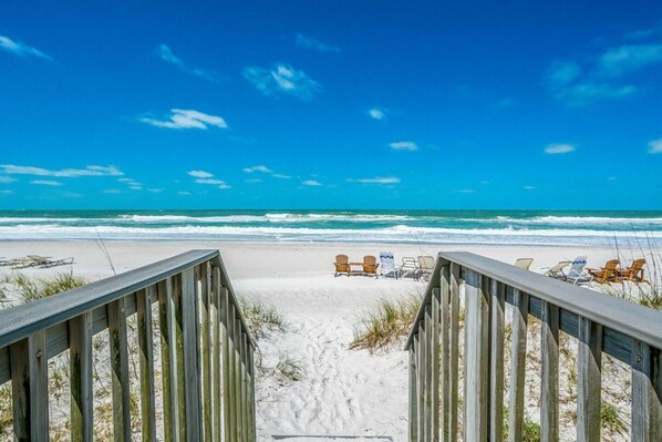 A wooden boardwalk leading to beach chairs on a sandy shore with a clear blue sky.