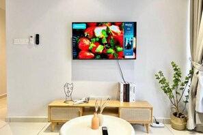 A modern living room with a flat-screen TV mounted on the wall, a wooden console table with a vase and a remote control, and a potted plant. - Gaia Residence, Gamuda Gardens Rawang by Sleepy Bear (Rawang)