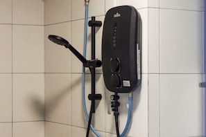 Um chuveiro DEKA preto fixado numa parede revestida de azulejos, com uma mangueira azul.