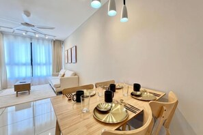 A modern dining area with a wooden table set for four, a ceiling fan, and a sofa in the background. - Gaia Residence, Gamuda Gardens Rawang by Sleepy Bear (Rawang)