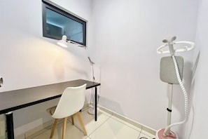 Quarto pequeno e moderno com escrivaninha, cadeira e poltrona de massagem.
