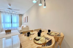 A modern dining area with a wooden table set for four, a ceiling fan, and a view of a living room with a sofa and a window. - Gaia Residence, Gamuda Gardens Rawang by Sleepy Bear (Rawang)