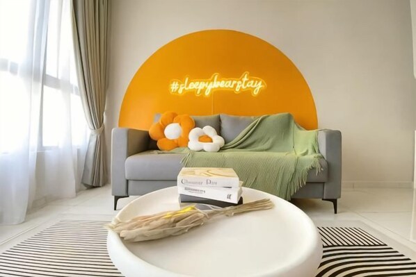 A living room with a sofa, a round coffee table, and a neon sign. - Gaia Residence, Gamuda Gardens Rawang by Sleepy Bear (Rawang)