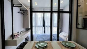 Una habitación de hotel moderna con un ventanal grande, una cama, una mesa con platos y una estantería con libros y una lámpara.