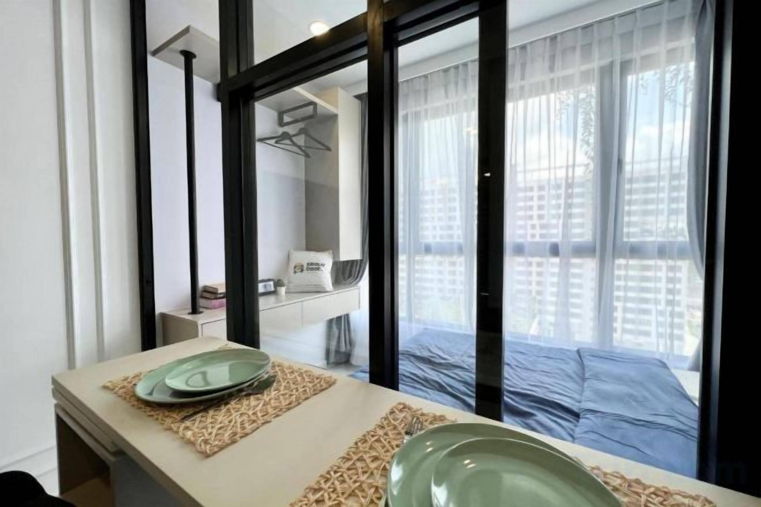 Une chambre d’hôtel avec une grande fenêtre, un lit, une table de chevet avec une assiette et un miroir.