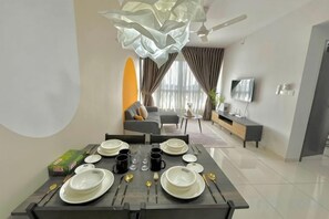 A dining area with a table set for four, a sofa, and a TV in the background. - Gaia Residence, Gamuda Gardens Rawang by Sleepy Bear (Rawang)