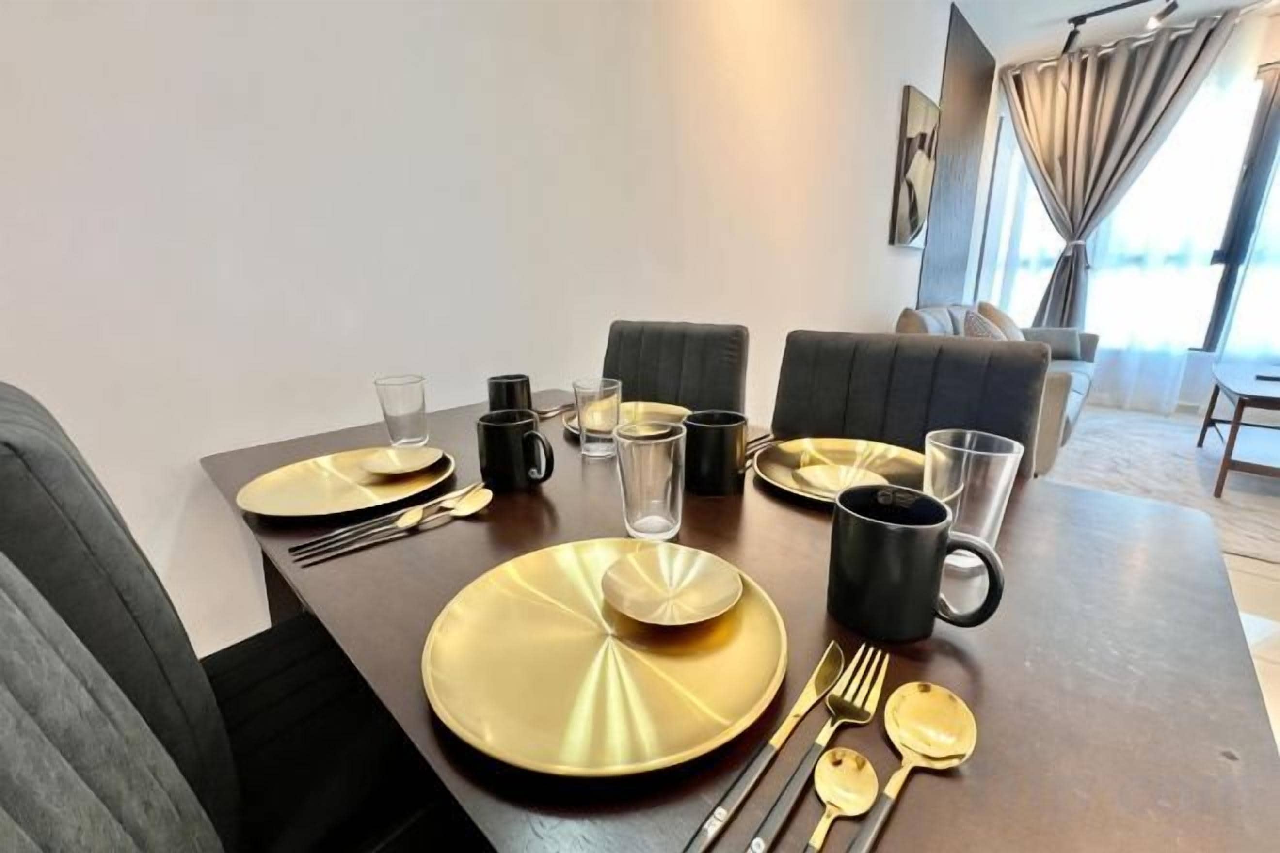 A dining table set with gold plates, cutlery, and black mugs, with a modern interior and a view of the outdoors.