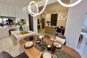 A modern kitchen with white cabinets, a dining area with a wooden table, and a glass partition separating the kitchen from the dining space.