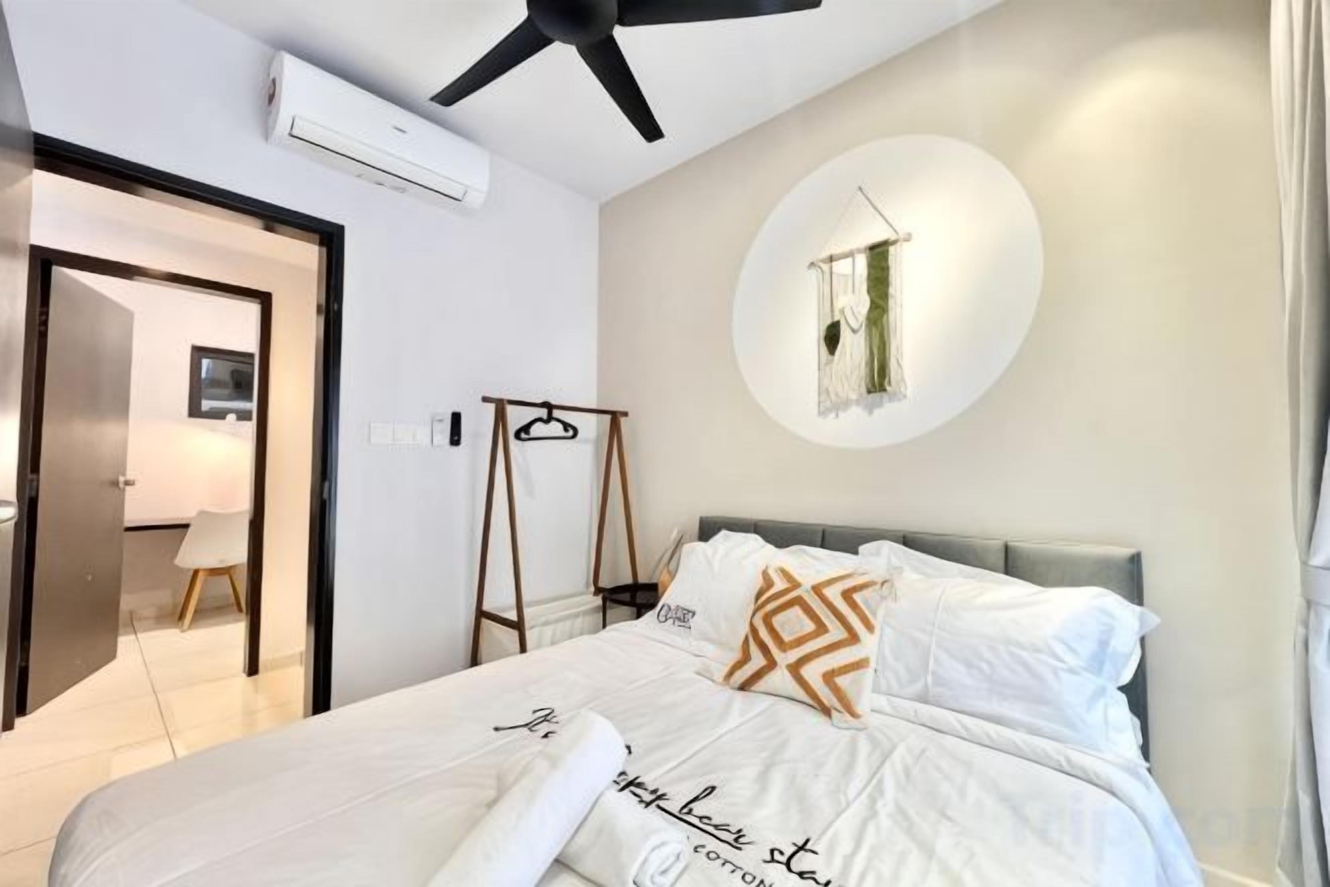 Un dormitorio con una cama, un ventilador de techo, una lámpara circular fijada a la pared y una puerta que da a otra habitación.