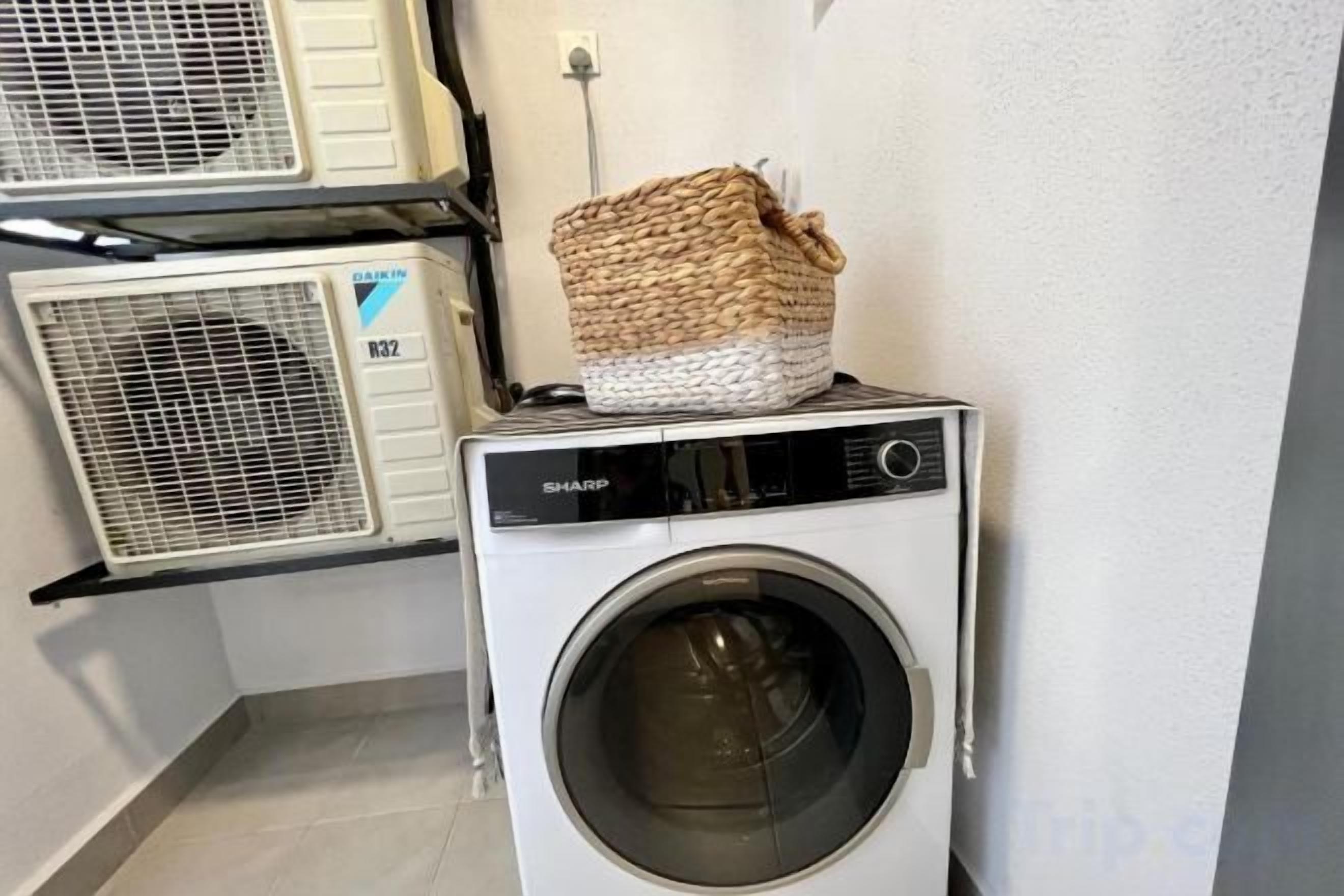 Una lavadora de carga frontal con una cesta encima, un aire acondicionado de pared y un tendedero.