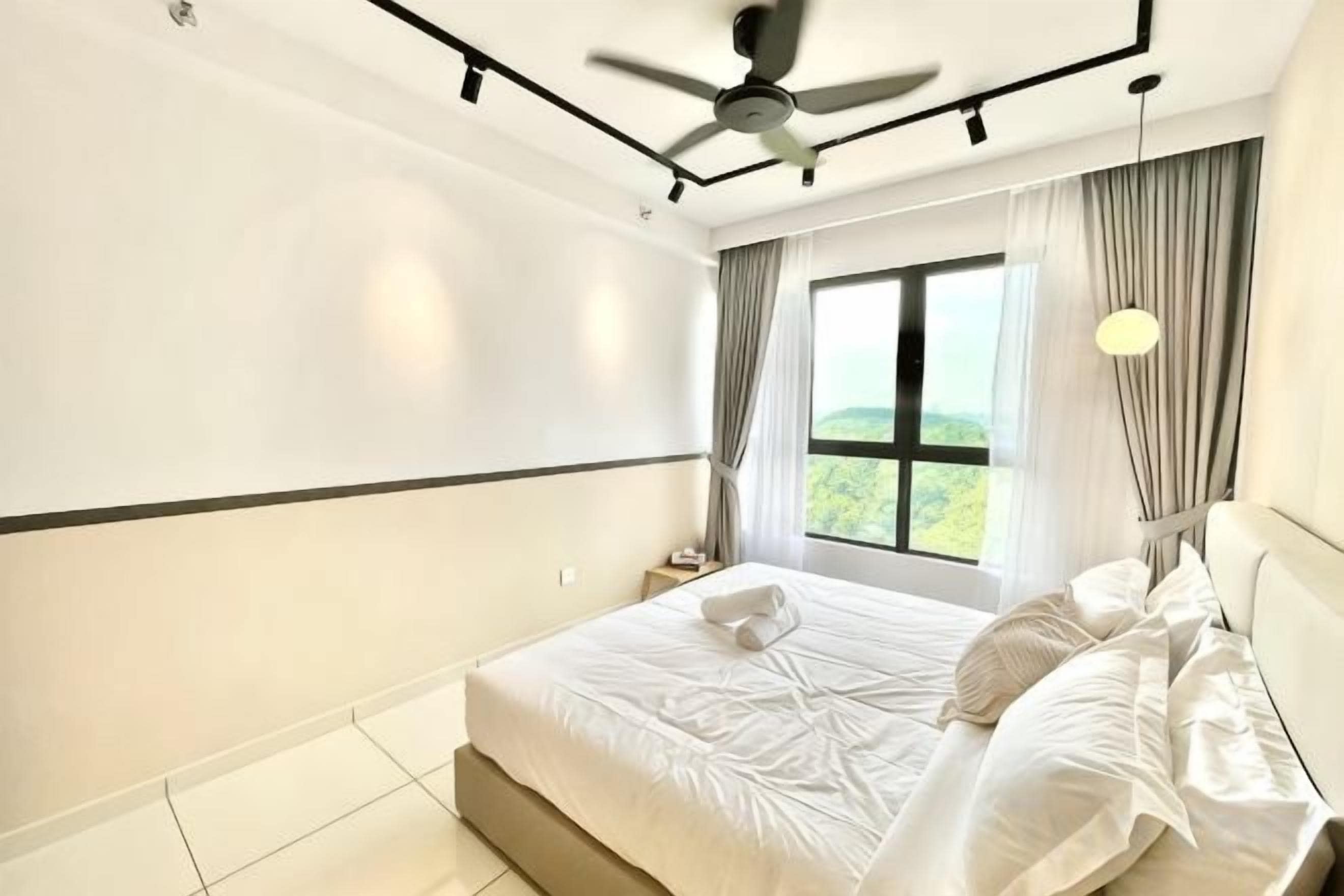 Un dormitorio con cama, ventilador de techo, mesita de noche, ventana con cortinas y vistas al exterior.