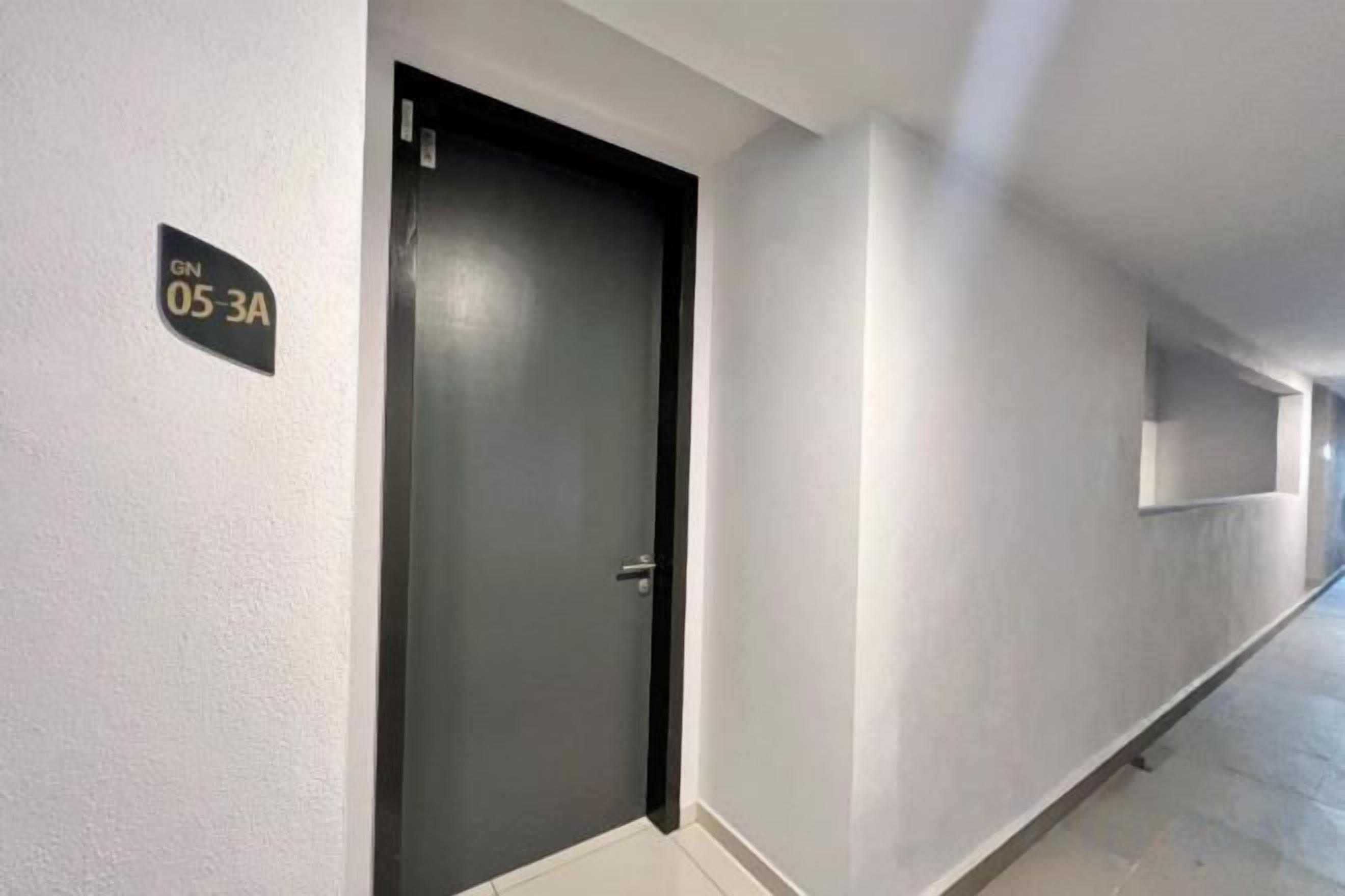 Un pasillo con una puerta cerrada, un letrero con un número y una lámpara en la pared.