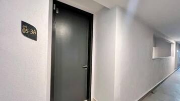 Un pasillo con una puerta cerrada, un letrero con un número y una lámpara en la pared.