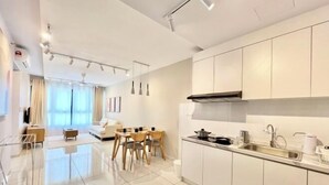 A modern kitchen with white cabinets, a stainless steel sink, and a dining area with a table and chairs. - Gaia Residence, Gamuda Gardens Rawang by Sleepy Bear (Rawang)