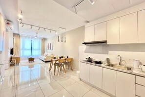 A modern kitchen with white cabinets, a stainless steel sink, and a dining area with a table and chairs. - Gaia Residence, Gamuda Gardens Rawang by Sleepy Bear (Rawang)