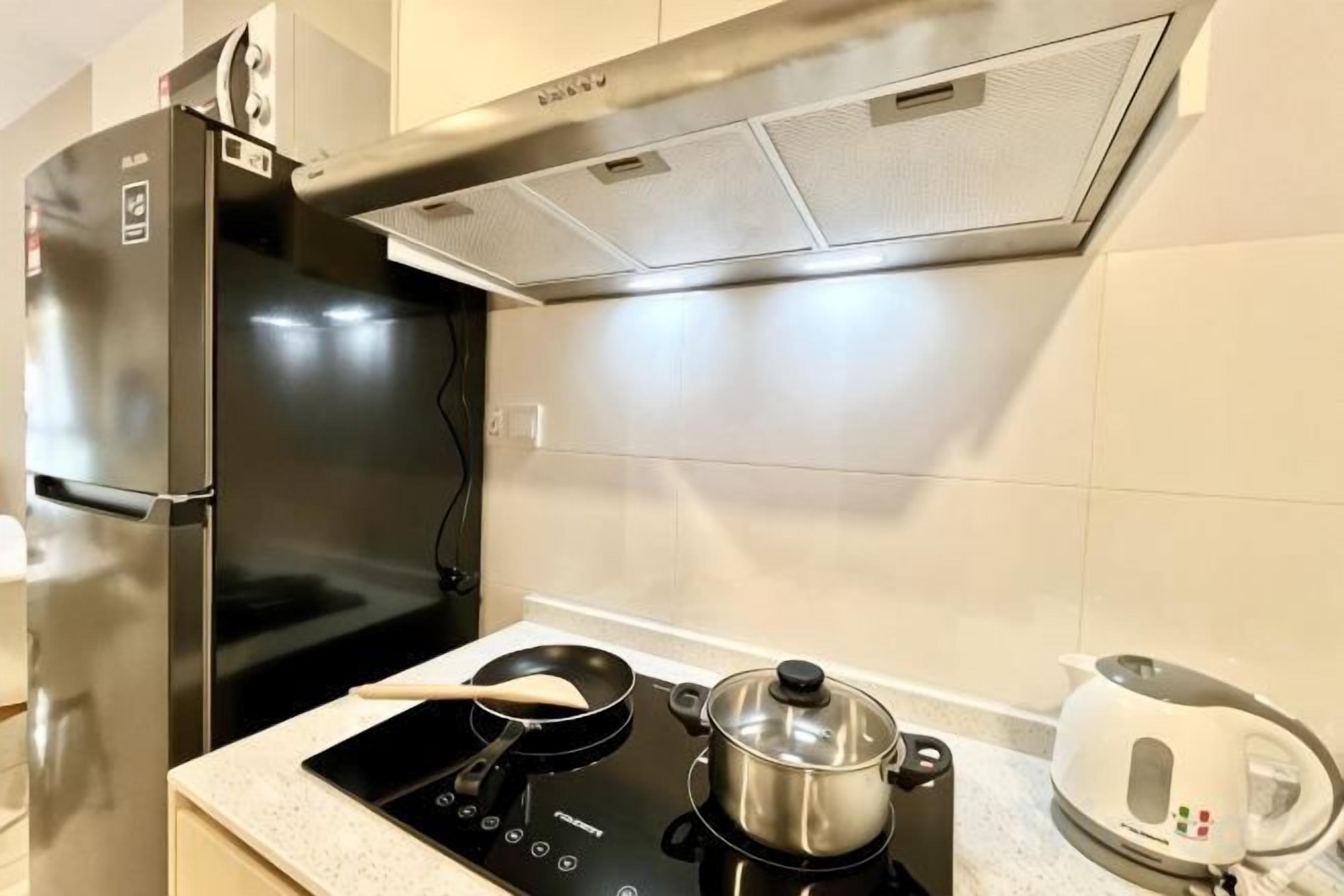 A kitchen with a black induction cooktop, a pot on it, a kettle, and a refrigerator.