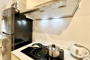 A kitchen with a black induction cooktop, a pot on it, a kettle, and a refrigerator. - Gaia Residence, Gamuda Gardens Rawang by Sleepy Bear (Rawang)