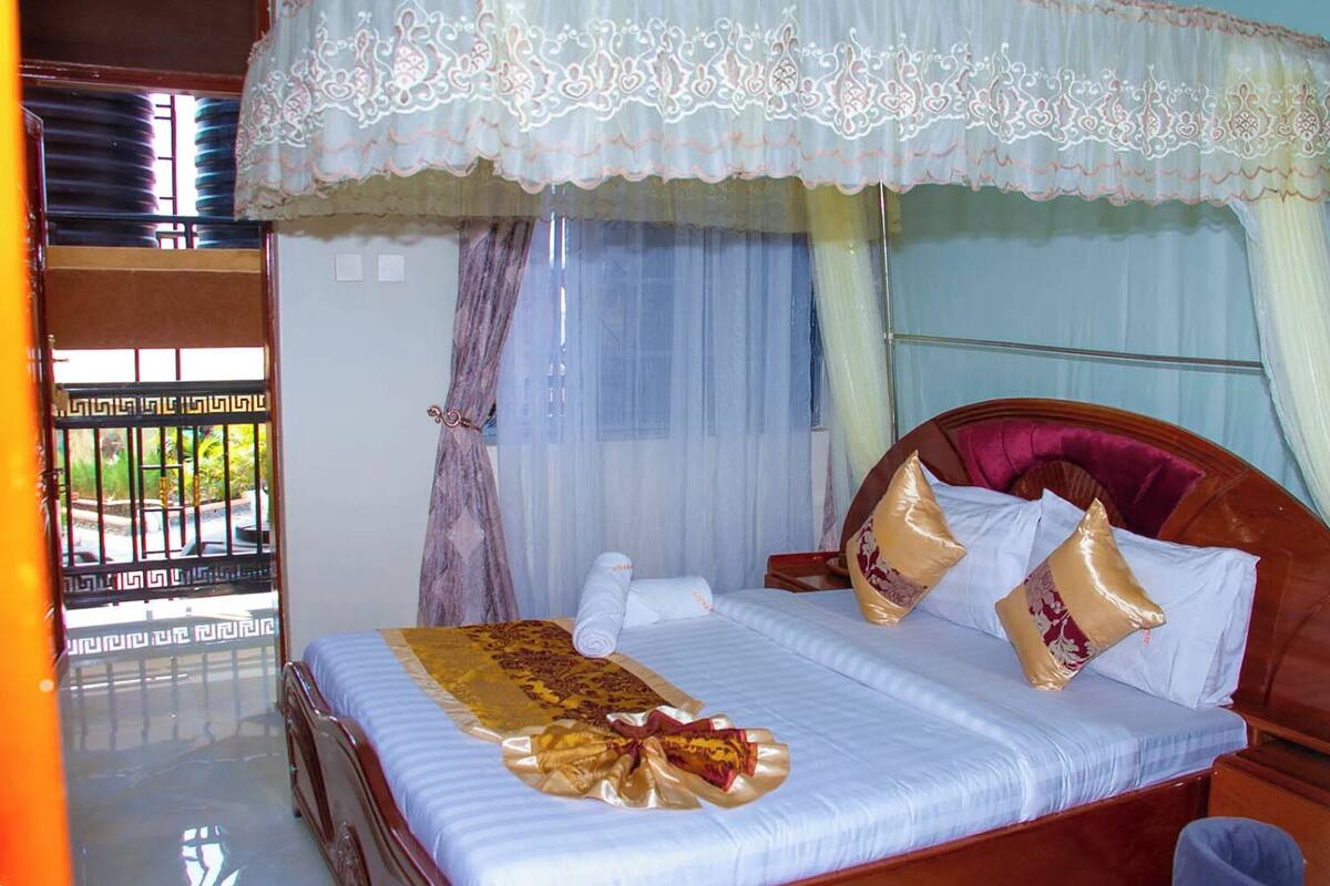 A bed with a canopy, a bedside table, and a window with curtains.