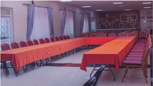 Uma sala de conferências com uma mesa comprida, fileiras de cadeiras e cortinas.