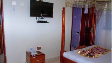 Un dormitorio con cama con dosel, una mesita de noche con teléfono y un televisor montado en la pared.