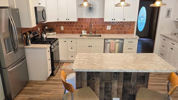 Una cocina moderna con armarios blancos, encimera de granito y una isla central con taburetes de bar.