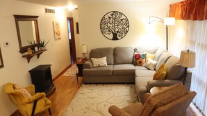 Una sala de estar con un sofá, sillones, una mesa de centro, una chimenea y un cuadro de pared con un árbol decorativo.
