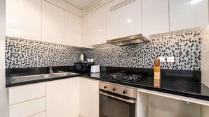 A modern kitchen with white cabinets, a black countertop, a gas stove, a microwave, and a sink. - Helnan Royale (Dubai)