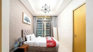A modern hotel room with a large bed, a bedside table with a lamp, a window with curtains, and a door. - Helnan Royale (Dubai)
