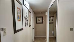 Un pasillo con cuadros en las paredes, suelo de baldosas y una puerta al final.