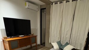 Um quarto moderno com uma cama de solteiro, uma escrivaninha de madeira, uma televisão e uma cortina.