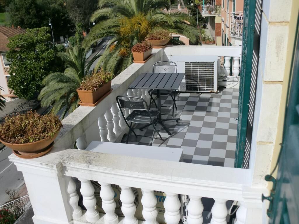Ein Balkon mit kariertem Boden, einem Tisch, Stühlen, Topfpflanzen und einer Klimaanlage.