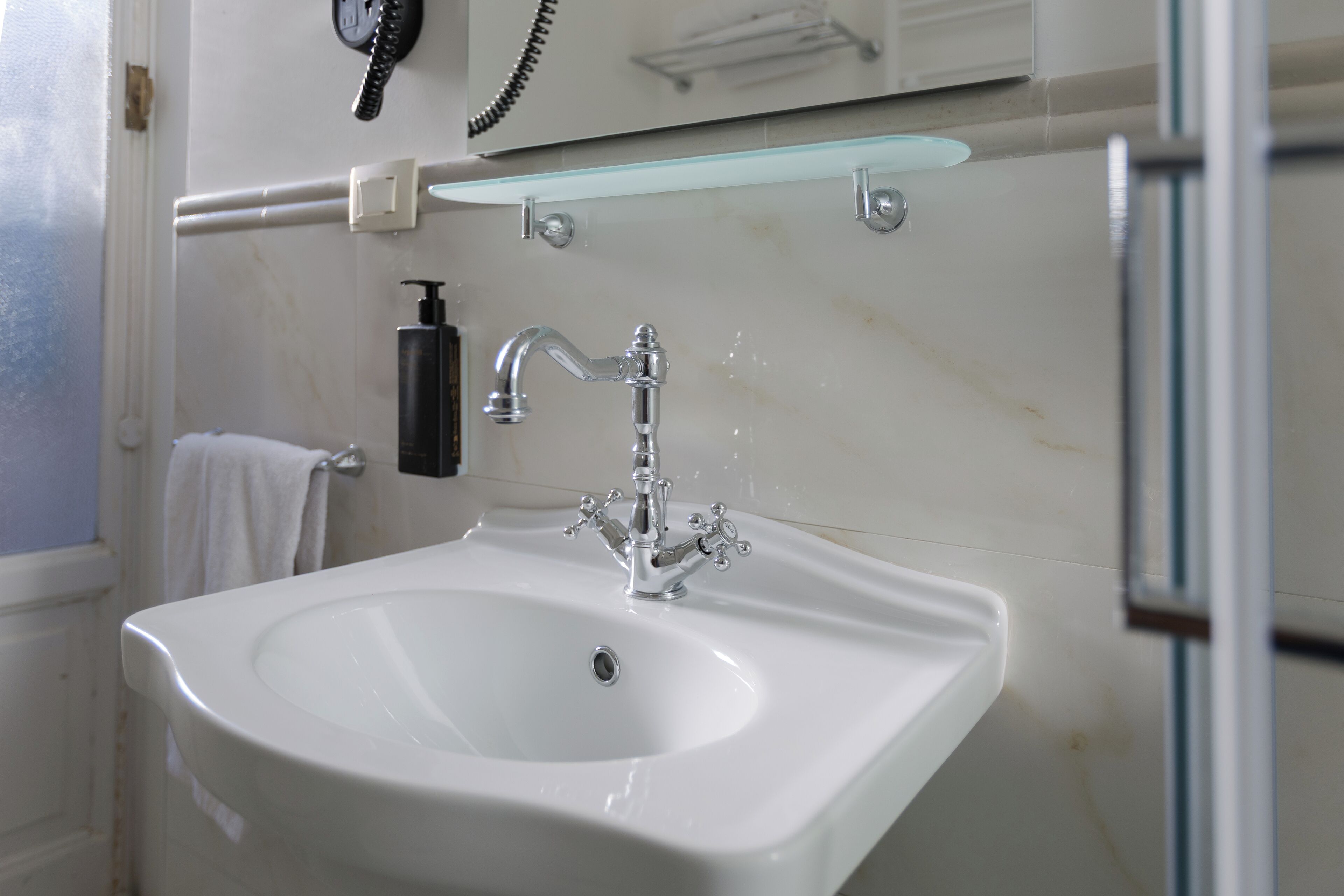 Une salle de bain avec un lavabo blanc, un miroir, une étagère en verre et un téléphone.