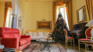A living room with a red sofa, a white armchair, a Christmas tree, a piano, and a painting on the wall. - Hotel Delle Rose Rapallo (Rapallo)