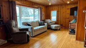A cozy living room with a wooden ceiling, a sofa, a chair, and a small table with a fan. - Peace Cottage on the Water-Rustic Charm & Lakefront Living!! (Faribault)