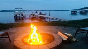A fire pit with a lake view, docked boats, and a wooden deck. - Peace Cottage on the Water-Rustic Charm & Lakefront Living!! (Faribault)