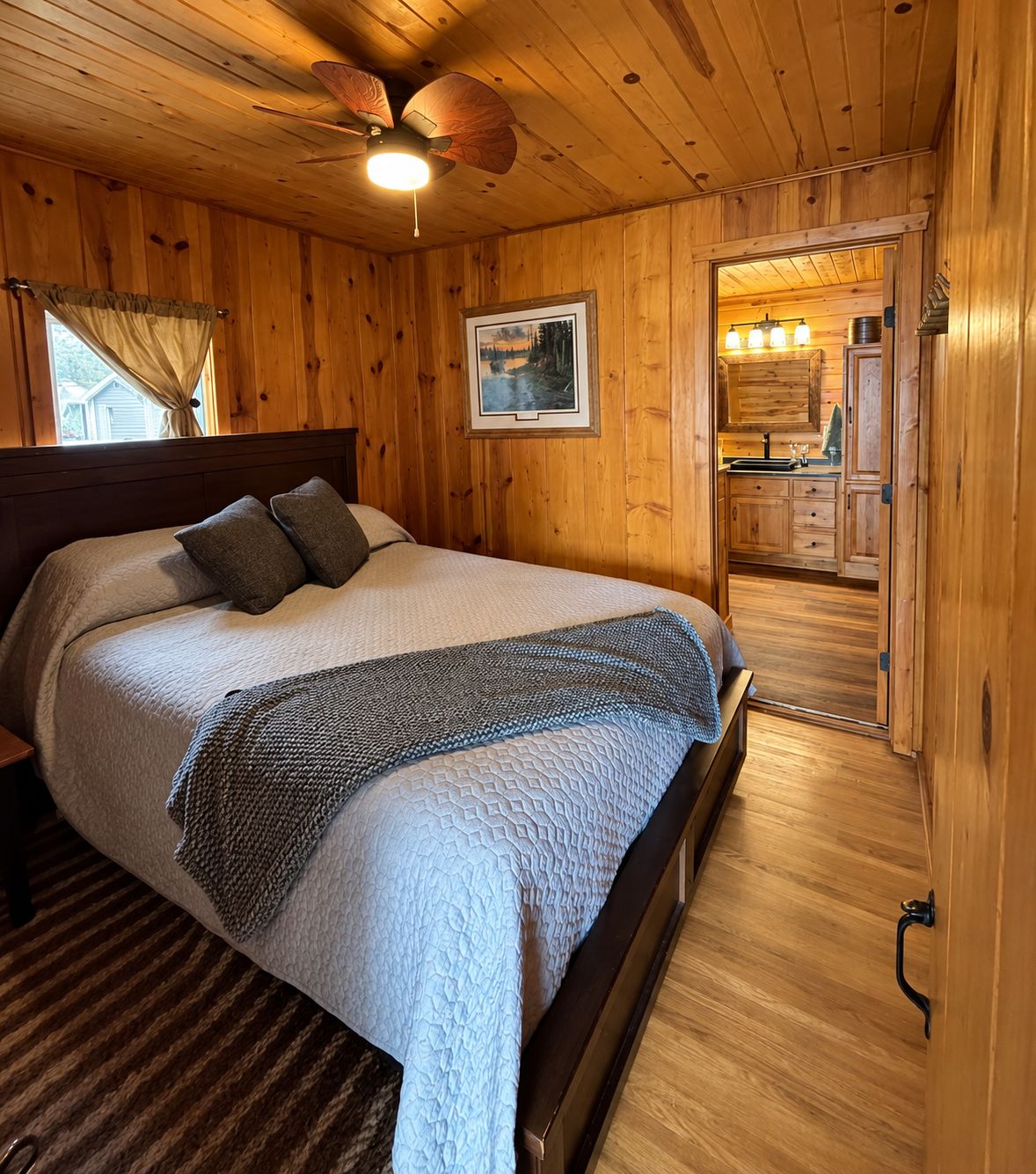 A wooden-paneled bedroom with a bed, a ceiling fan, and a framed picture on the wall.