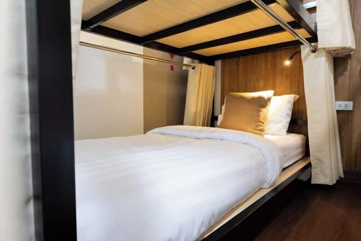 Ein Einzelbett mit weißer Bettwäsche, einem Holz-Kopfteil und einem Vorhang.