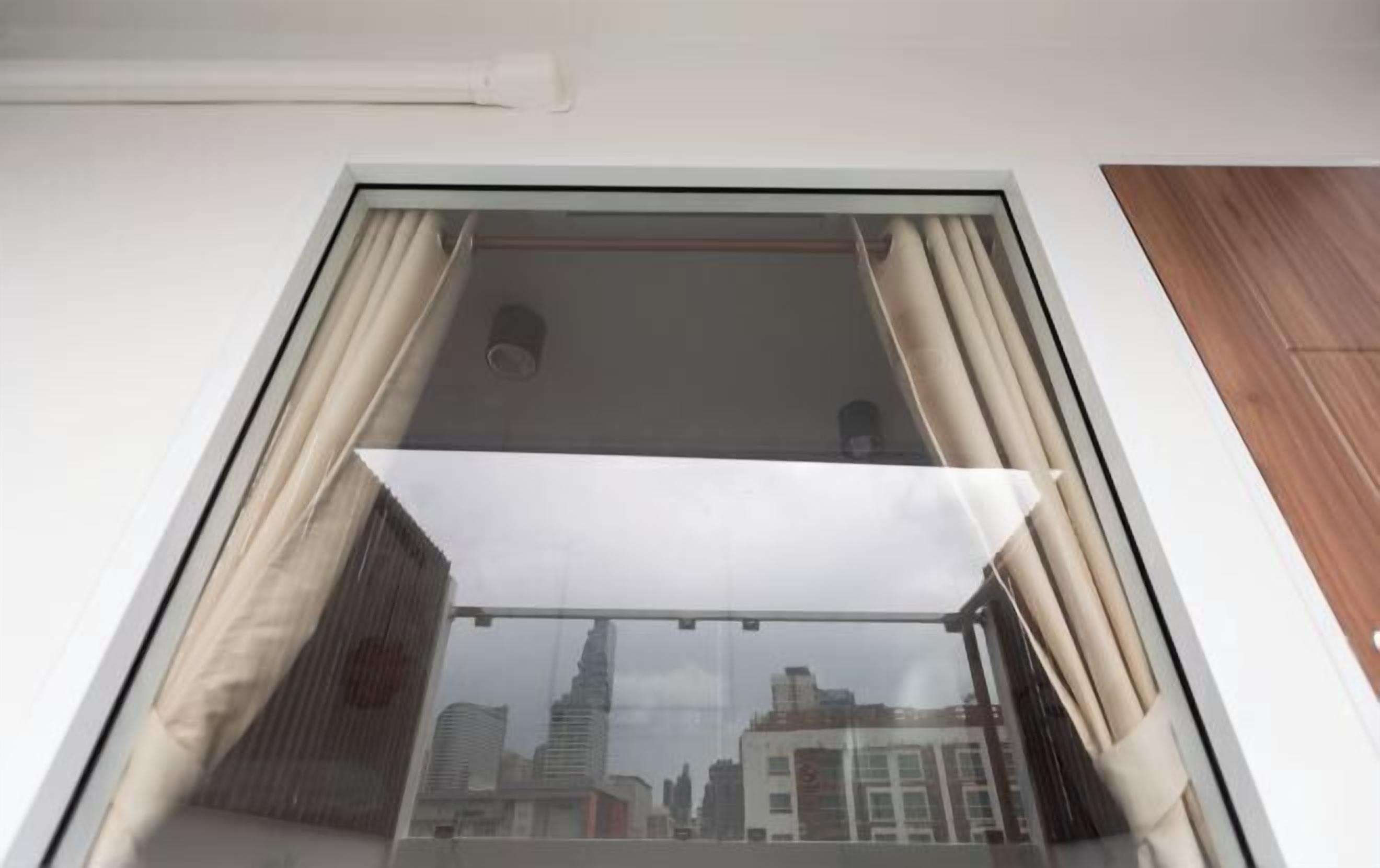 A window with a view of a cityscape, curtains, and a ceiling vent.