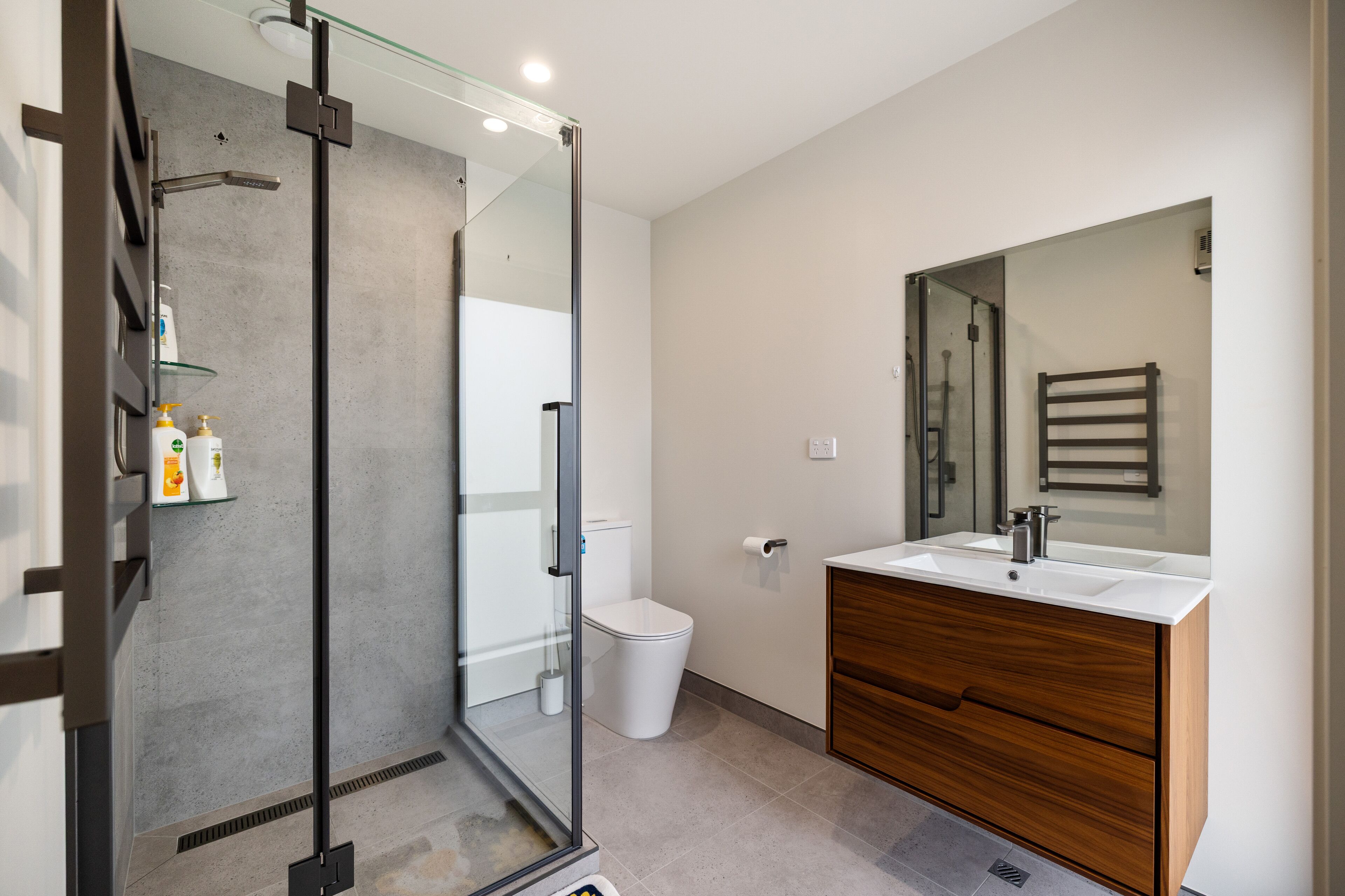 A modern bathroom with a glass-enclosed shower, a white sink, and a wooden vanity.