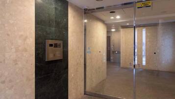 Um elevador moderno com painel de controle, porta de vidro e corredor que dá para outro cômodo.