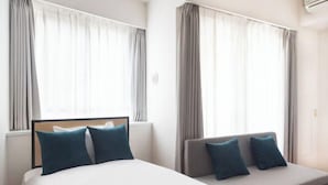 A hotel room with a bed, a sofa, and large windows with curtains. - Daffitto Tennozu (Tokyo)