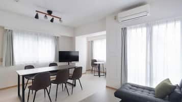 Uma sala de estar moderna com área de jantar, televisão de tela plana e uma grande janela com cortinas.