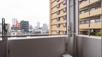 Uma varanda com grades de metal, uma janela e vista para um horizonte urbano com edifícios.
