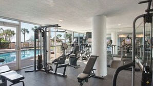 A gym with various exercise equipment, a pool, and large windows offering a view of palm trees. - 🦩Book Me Baby! Beach Penthouse at Pelican Beach🦩 (Destin)