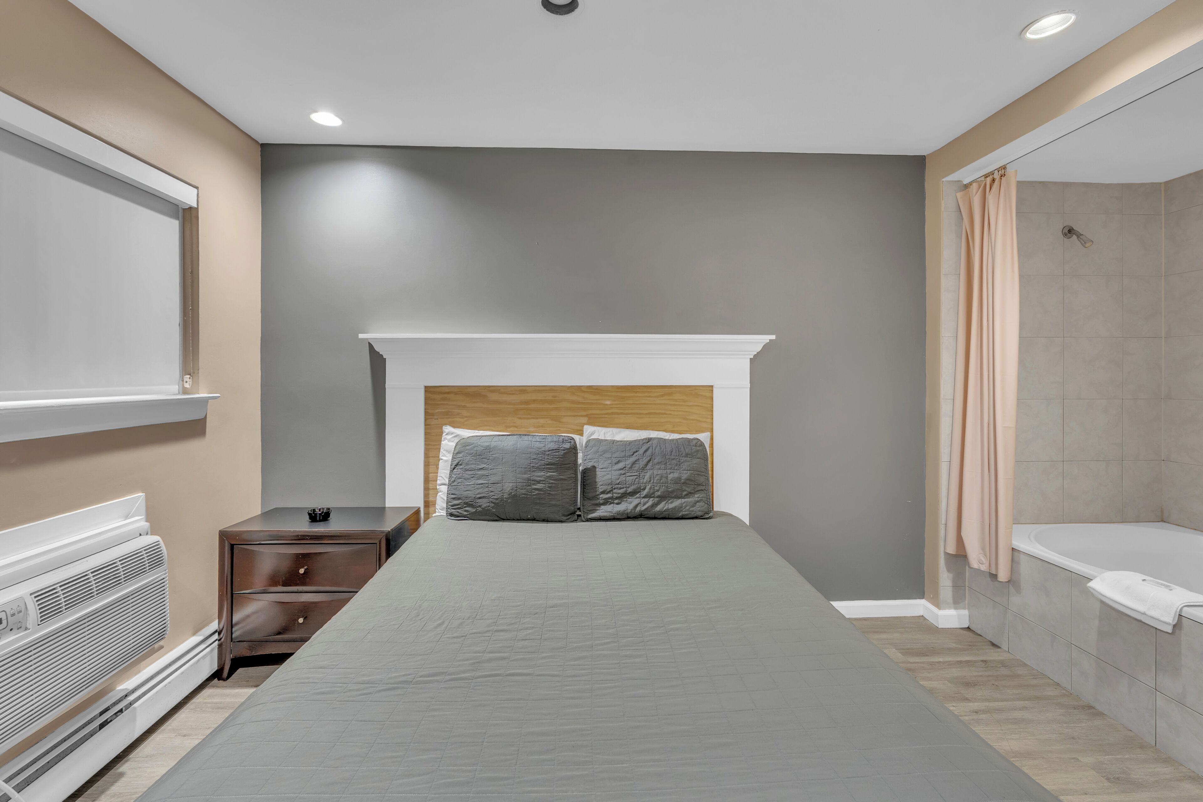 A bedroom with a bed, a nightstand, a heater, and a shower area.