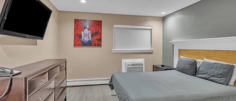 A bedroom with a bed, dresser, TV, artwork, and an air conditioning unit.