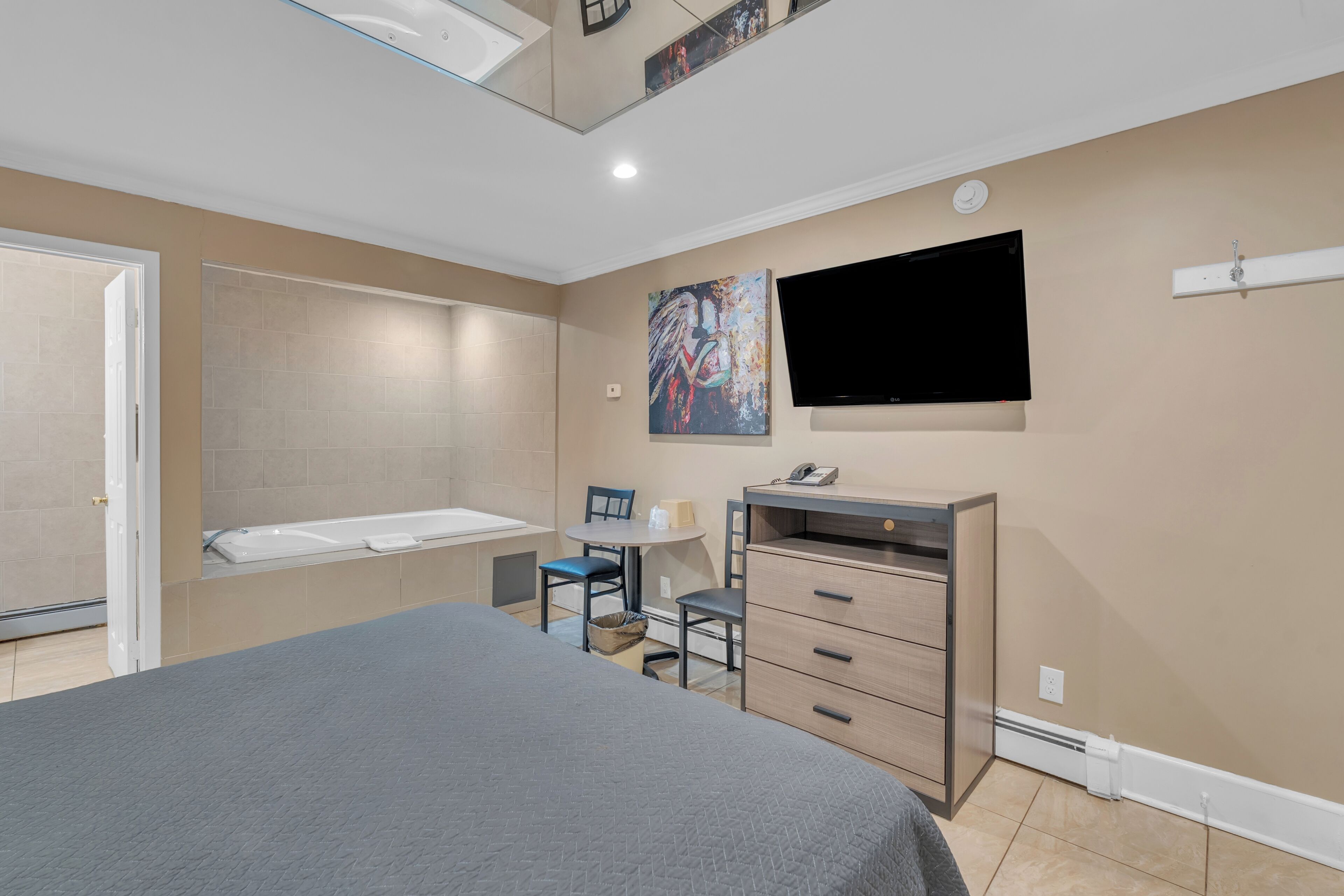 A bedroom with a bed, a desk, a chair, a television, and a bathroom with a bathtub.